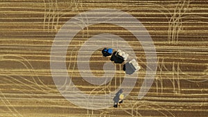 Aerial view of tractor as pulling trailer full with round bales of straw