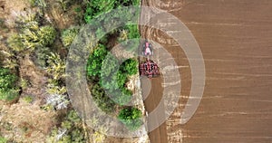 aerial view on tractor cultivator or seeder plows the land, prepares for crops on farming field near forest