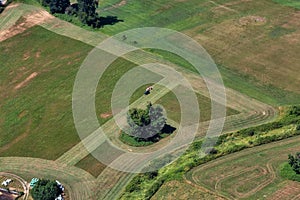 Aerial View of a tractor cutting the green grass field in a farm.