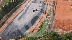 Aerial view of a tractor, dump trucks and a large pile of granite rubble.