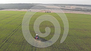 Aerial view of the tractor fertilising the chemicals on the large green field.