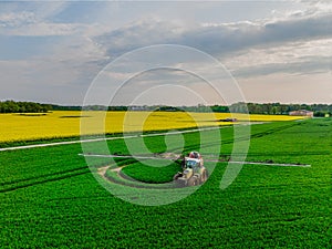 Aerial view of tractor with fertilizer spreader in wheat field.