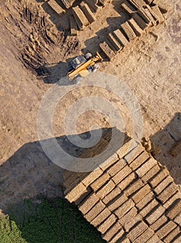 Aerial view of a tractor folding bales of hay in a field on a sunny autumn day. Photo from drone. Top view