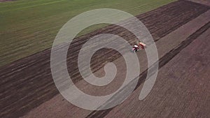 Aerial view of tractor with mounted seeder performing direct seeding of crops on plowed agricultural field.