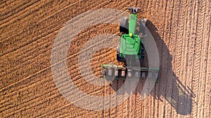 Aerial view of tractor with mounted seeder performing direct seeding of crops on plowed agricultural field. Farmer is