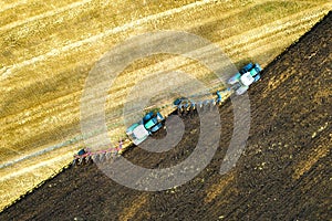 Aerial view of a tractor plowing black agriculture farm field after harvesting in late autumn