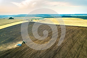 Aerial view of a tractor plowing black agriculture farm field after harvesting in late autumn