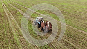 Aerial view of a tractor with a round baler which makes bales of straw on a harvested field, a concept of agribusiness