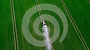 Aerial view of the tractor spraying the chemicals on the large green field