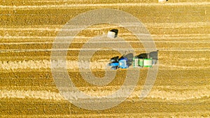 Aerial view of tractor tow trailed bale machine to collect straw from harvested field