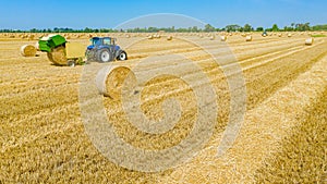 Aerial view of tractor tow trailed bale machine to collect straw from harvested field