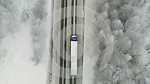 Aerial view of traffic on the road passing through the winter forest in severe weather. Scene. Top view of a cargo truck