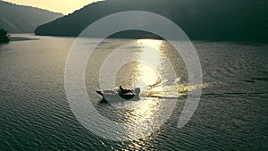 Aerial view Tranquil River Sunset with Boat, A boat glides on a river shimmering with the golden light of the setting