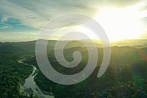 Aerial view of a tropical river meandering through the rainforest during sunset with sunrays covering the forest