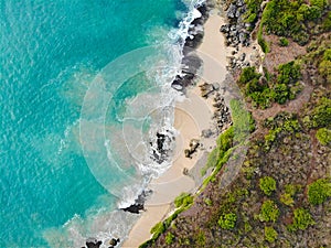 Aerial view of tropical sand beach with rocks and green cliff