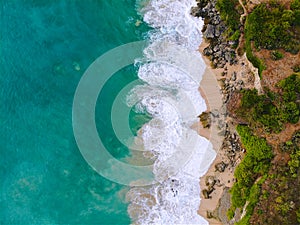 Aerial view of tropical sand beach with rocks and green cliff