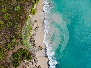 Aerial view of tropical sand beach with rocks and green cliff
