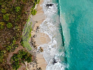 Aerial view of tropical sand beach with rocks and green cliff