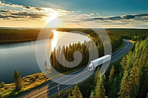 Aerial view of a truck driving along the road through the forest at sunset. Aerial view of semi truck with cargo trailer on road