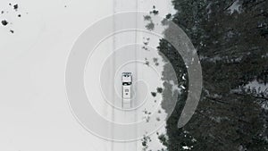 Aerial view of a truck driving on a road surrounded by winter forest. Clip. Cargo truck moving on a snow covered road
