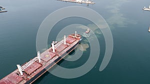 Aerial view of tug boat assisting big cargo ship. Large cargo ship enters the port escorted by tugboats