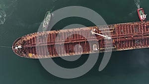 Aerial view of tug boat assisting big oil tanker. Large oil tanker ship enters the port escorted by tugboats.