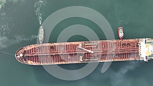 Aerial view of tug boat assisting big oil tanker. Large oil tanker ship enters the port escorted by tugboats.