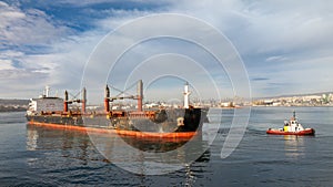 Aerial view of Tug boats assisting big cargo ship. Large cargo ship enters the port escorted by tugboats