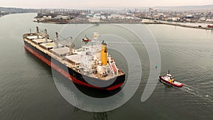 Aerial view of Tug boats assisting big cargo ship. Large cargo ship enters the port escorted by tugboats