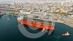 Aerial view of tug boats assisting big oil tanker. Large oil tanker ship enters the port escorted by tugboats