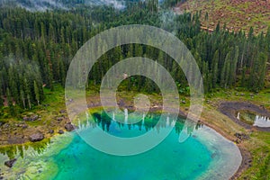 Aerial view of turquoise blue water of lake Carezza in Alps Dolomites. Lago di Karersee near fir tree forest