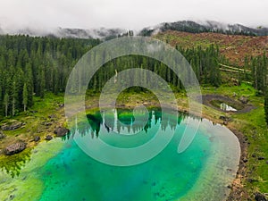 Aerial view of turquoise blue water of lake Carezza in Alps Dolomites. Lago di Karersee near fir tree forest