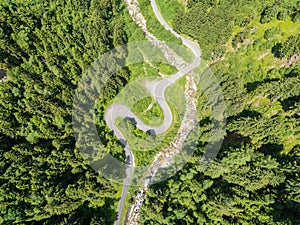 Aerial view of twisty road in the Alps with a small river and Bridge. Trees and road seen from top down. Strong green colors
