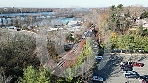 Aerial view of two car light rail train stopped at a station with passengers getting off and on near a busy highway bridge over a