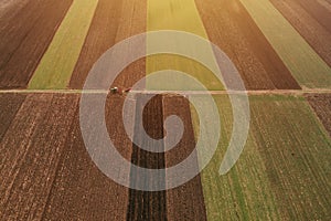 Aerial view of two farm tractors tilling in cultivated fields