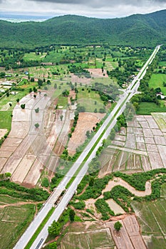 Aerial view of two-lane road through paddy fields and mountain range in rainy