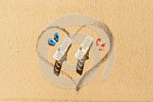 Aerial view of two pair of flip flops, sunbed in shape of heart on sandy tropical beach. Valentines day. Holiday concept. Creative