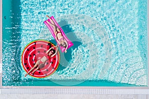 Aerial view of two women floating on inflatable mattresses relaxing in the swimming pool. Summer vocation