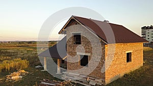 Aerial view of unfinished house with wooden roof structure covered with metal tile sheets under construction.