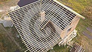 Aerial view of unfinished house with wooden roof structure covered with metal tile sheets under construction.