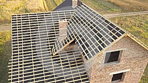 Aerial view of unfinished house with wooden roof structure covered with metal tile sheets under construction.