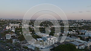 Aerial view of urban borough at twilight. Fly above buildings and streets in city, downtown skyscrapers in distance.