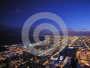 aerial view of the urban landscape of Chicago and Lake Michigan at night with vibrant lights, modern architecture, and clouds.