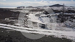 Aerial view of the vehicle driving in winter high hills on cloudy sky background. Clip. Hiking in cold weather, minivan