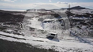 Aerial view of the vehicle driving in winter high hills on cloudy sky background. Clip. Hiking in cold weather, minivan