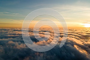 Aerial view of vibrant yellow sunrise over white dense clouds with blue sky overhead