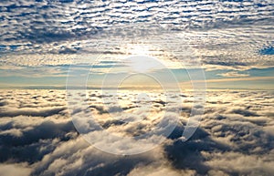 Aerial view of vibrant yellow sunrise over white dense clouds with blue sky overhead