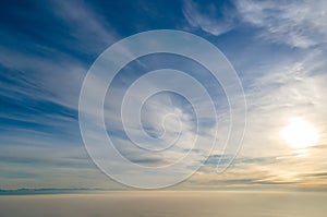 Aerial view of vibrant yellow sunrise over white dense clouds with blue sky overhead