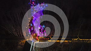 Aerial View Of A Vibrantly Lit Train Emitting Purple Smoke As It Passes Through A Forested Area At Night.