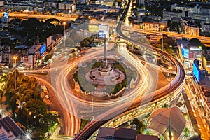Aerial view of Victory Monument with car light trails on busy street road. Roundabout in Bangkok Downtown Skyline. Thailand.